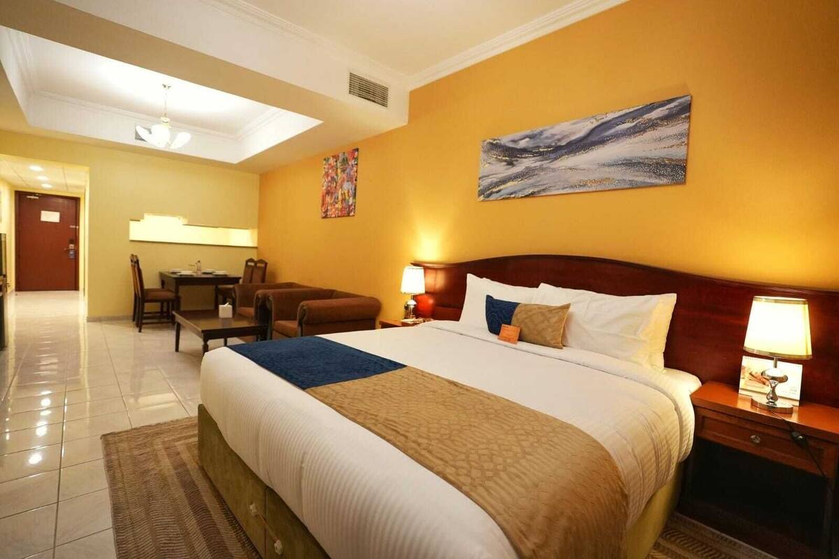 A hotel room with a large bed, a desk, a chair, and a painting on the wall.