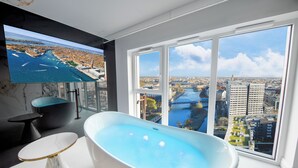 A modern bathroom with a freestanding bathtub, a marble-topped table, and a large window offering a city view. - Quorum Apartments (Wroclaw)