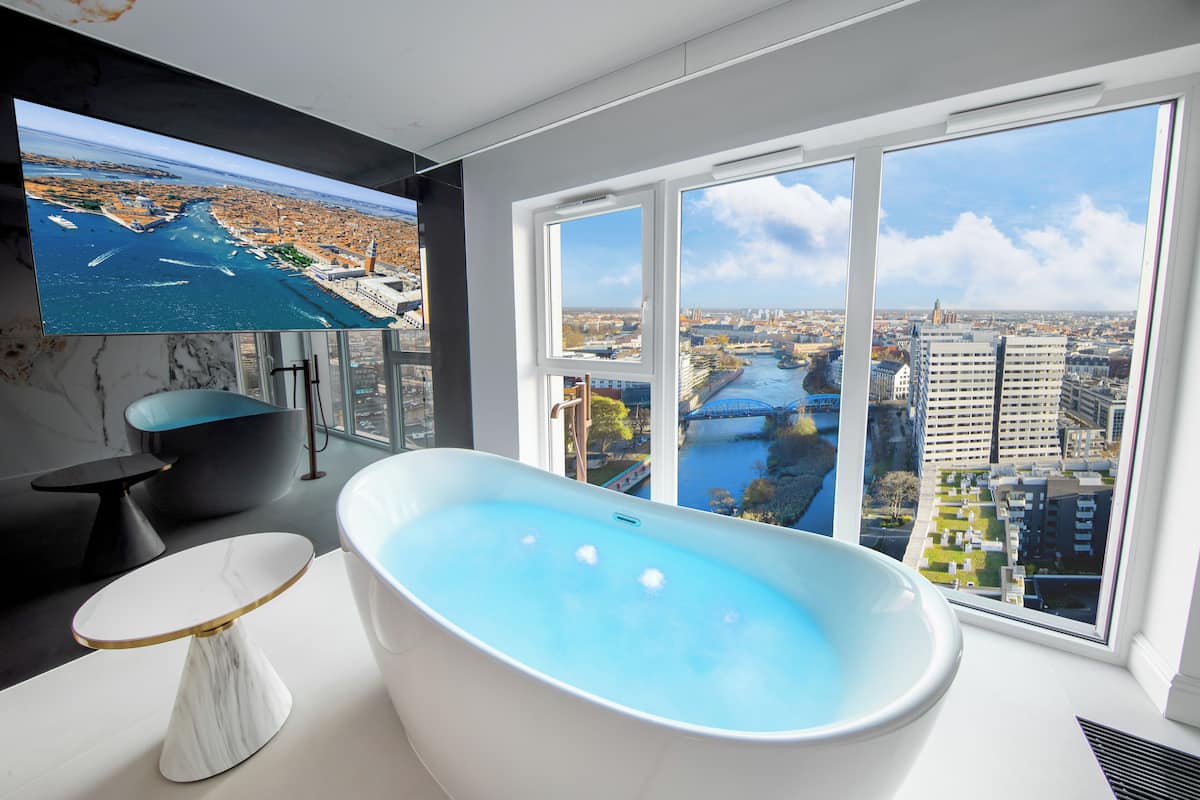 Ein modernes Badezimmer mit freistehender Badewanne, einem Tisch mit Marmorplatte und einem großen Fenster mit Blick auf die Stadt.