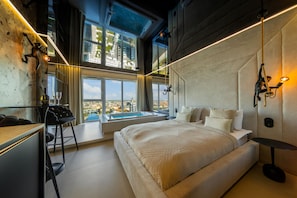 Ein modernes Schlafzimmer mit einem großen Bett, Blick auf die Stadt, einem Schreibtisch und einer Badewanne.