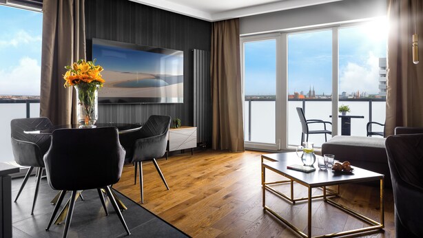 A modern living room with a large TV, comfortable seating, a wooden floor, and a view of the city. - Quorum Apartments (Wroclaw)