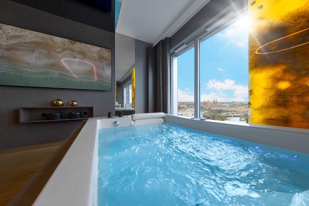 Ein modernes Badezimmer mit einer großzügigen Badewanne, Blick auf die Stadt und einem Bild an der Wand.