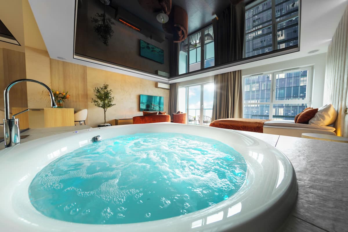 Ein modernes Hotelzimmer mit einer großen Whirlwanne, einem Essbereich und Blick auf die Stadtlandschaft.