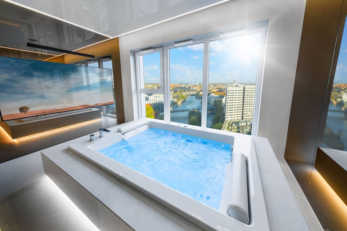 Ein modernes Badezimmer mit einer großen Badewanne, einer Duschkabine aus Glas und Blick auf die Stadt durch bodengrosse Fenster.