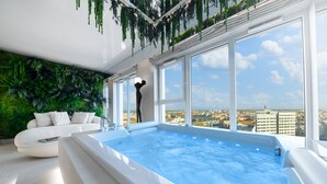 A modern indoor swimming pool with a city view, a white sofa, and lush green walls. - Quorum Apartments (Wroclaw)