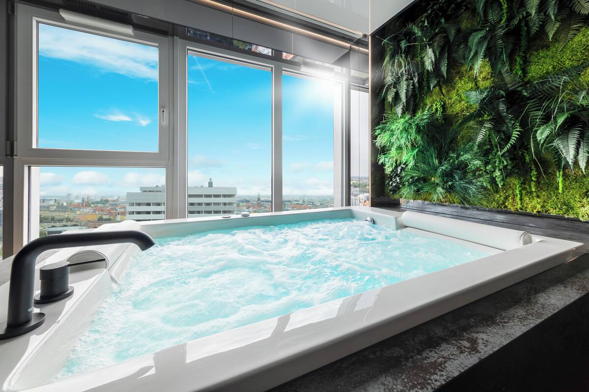 Ein Whirlpool mit Blick auf die Stadt durch große Fenster, umgeben von einer üppigen Grünwand.