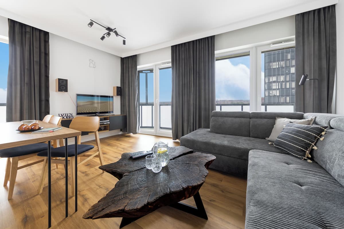 Ein modernes Wohnzimmer mit grauem Sofa, einem Holztisch und einem Essbereich mit Tisch und Stühlen.