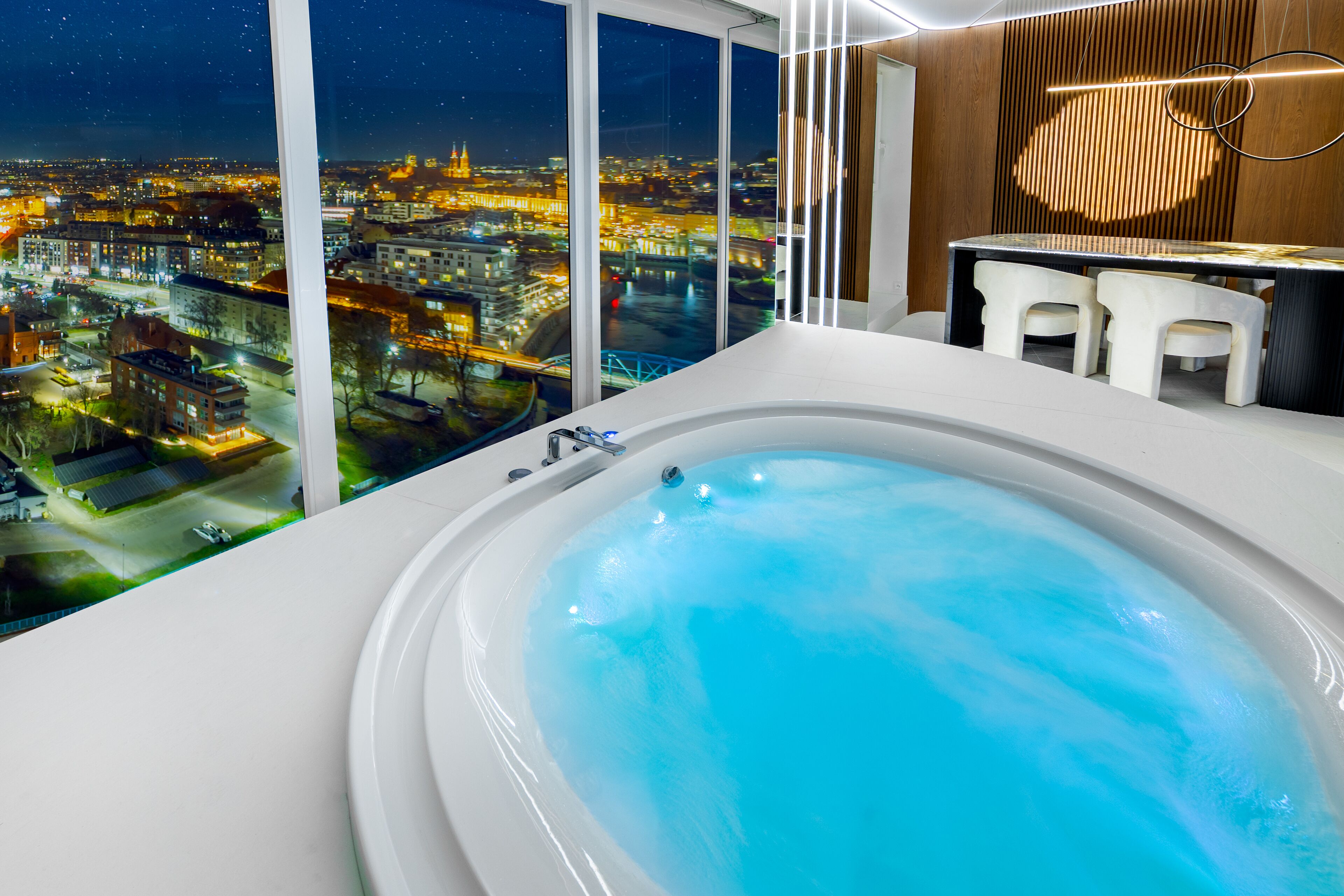 A modern bathroom with a large bathtub, a wooden panel wall, and a city view through large windows.