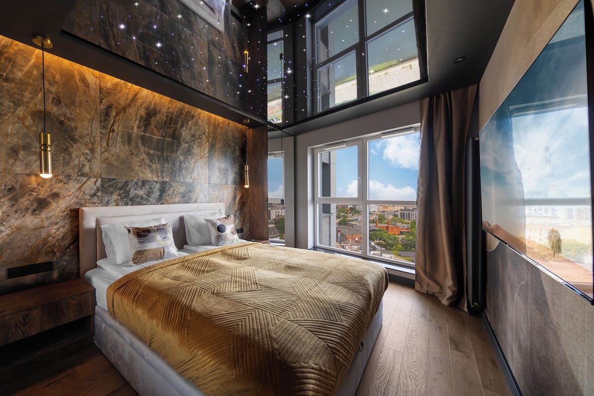 Ein modernes Schlafzimmer mit einem großen Bett, einer Marmorwand, Blick auf die Stadt und einem Sternenhimmel-Effekt.