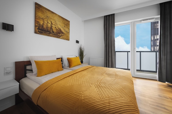 A modern bedroom with a large bed, a painting on the wall, and a view of the sky through the window. - Quorum Apartments (Wroclaw)