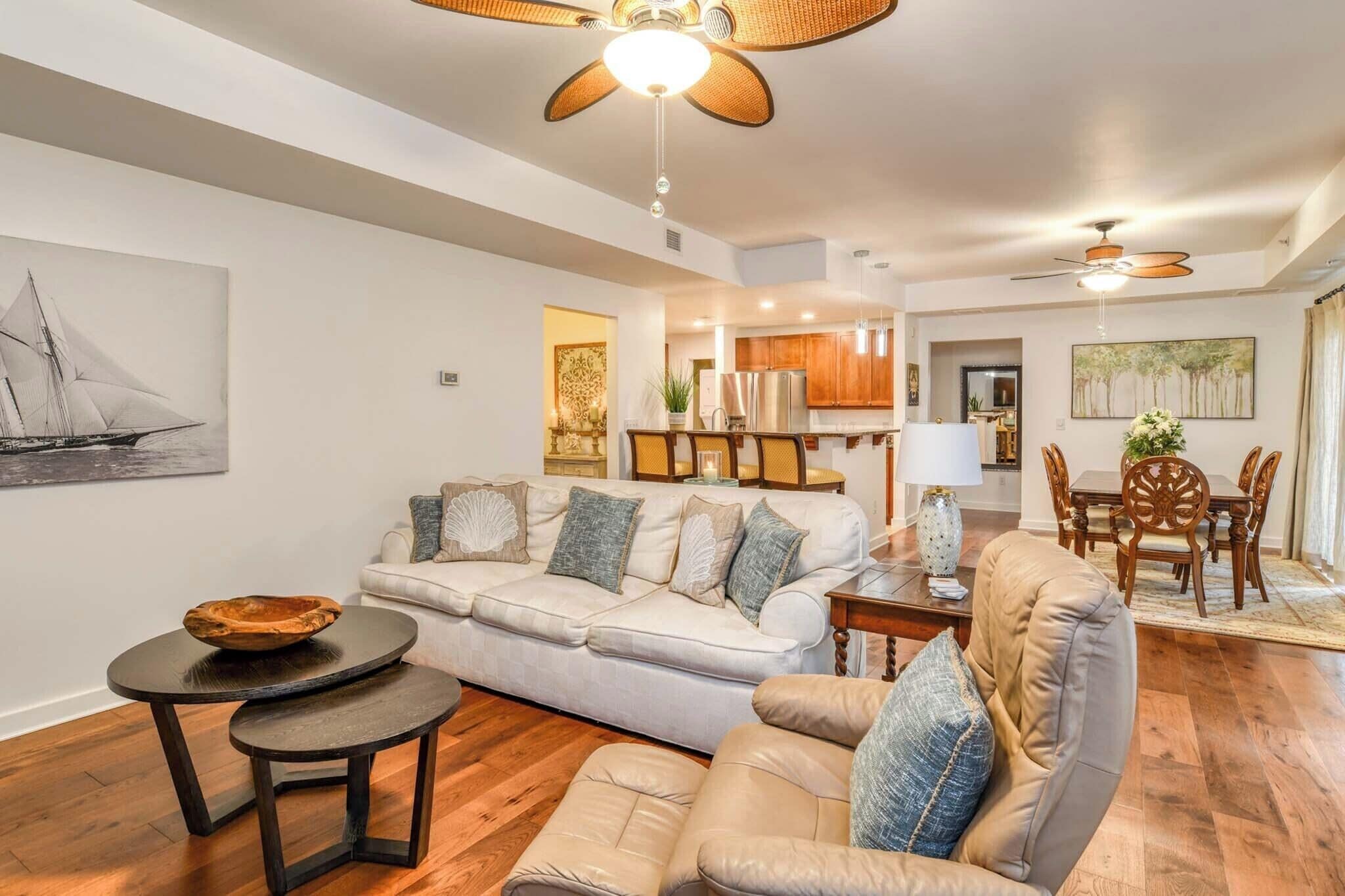 A spacious living room with a white sofa, a round coffee table, and a leather armchair. A dining area with wooden furniture is visible in the background.