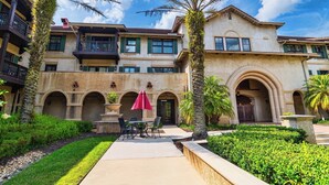 Un edificio a più piani con un cortile con palme, una zona pranzo con posti a sedere all'aperto e un grande ingresso ad arco.