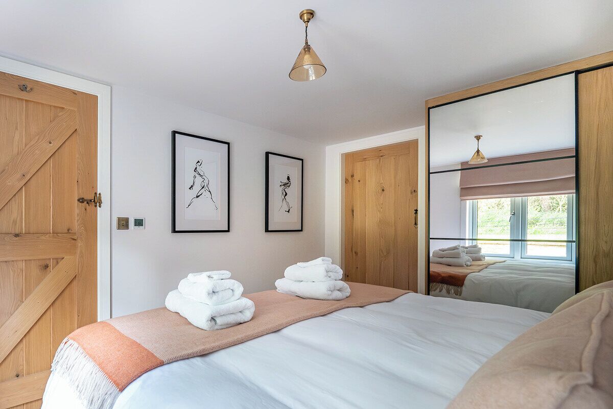 Un dormitorio con una cama grande, dos cuadros enmarcados, una puerta de madera y un espejo que refleja la habitación.