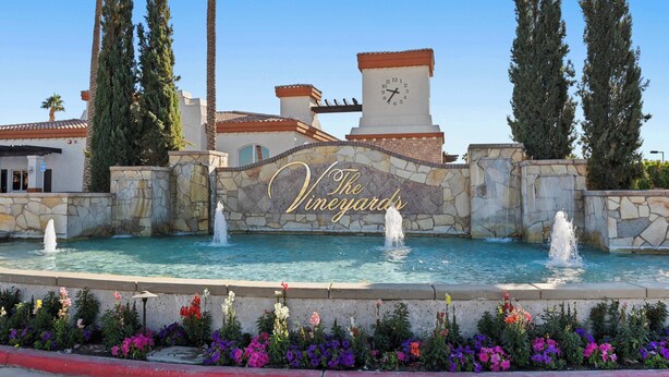 Une fontaine avec des jets d’eau, entourée d’un mur de pierre et d’une pancarte indiquant : « Les vignobles ».