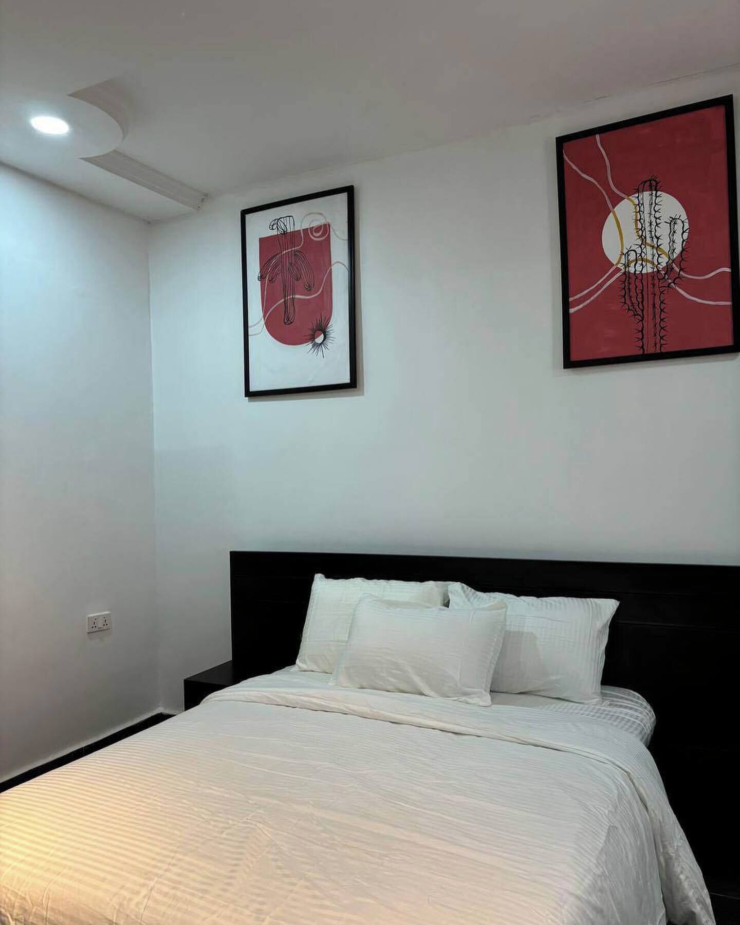 A bedroom with a bed, white bedding, a black headboard, and two framed artworks on the wall.