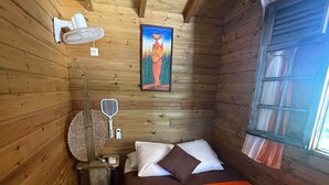 Acogedora habitación de cabaña de madera con cama, ventilador de pared, un cuadro y ventana con cortinas.