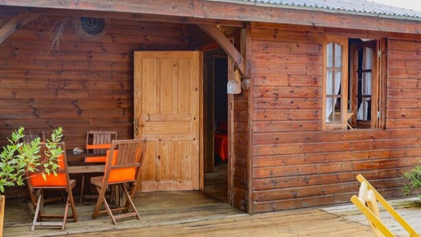Una cabaña de madera con un porche de madera, una mesa y sillas, y una ventana.