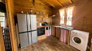 Una cocina compacta con paredes de madera, un refrigerador, un microondas, un lavabo y una lavadora.