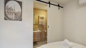 Ein Hotelzimmer mit Bett, einem Badezimmer inklusive Handtuchhalter und Blick auf den Eiffelturm durch ein Fenster.