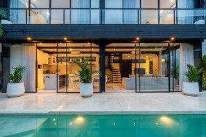 A modern house with a pool, large windows, and a staircase leading to an upper level.