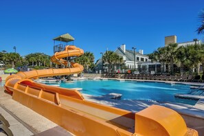 Ein Pool mit Wasserrutsche, Palmen und ein Gebäude mit Balkon im Hintergrund.