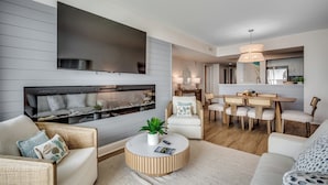 A modern living room with a flat-screen TV, a fireplace, a dining area, and a kitchen in the background. - 🌴Large Oceanfront~Lazy River~Awesome Amenities~ Caribbean Resort 1105🌴 (Myrtle Beach)