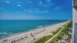 A beach with umbrellas, a pier, and a view of the ocean. - 🌴Large Oceanfront~Lazy River~Awesome Amenities~ Caribbean Resort 1105🌴 (Myrtle Beach)