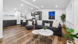 A modern living room with a grey sofa, a coffee table, and a kitchen in the background.