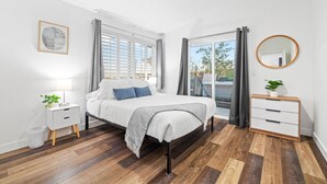 A modern bedroom with a large bed, a bedside table with a lamp, a dresser, and a round mirror.