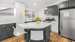 A modern kitchen with white cabinets, a central island with chairs, a stove, microwave, and refrigerator.