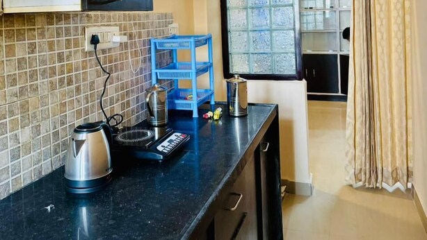 A compact kitchen with a black countertop, a blue shelf, and a window with a view of the outside. - Luxe Heaven (Jaipur)