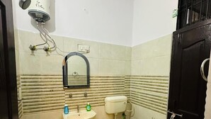 A small bathroom with a sink, toilet, and a mirror. There is a water heater mounted on the wall. The walls are tiled with a beige and white pattern. - Luxe Heaven (Jaipur)
