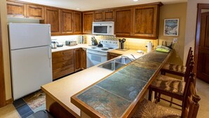 A kitchen with wooden cabinets, a refrigerator, a microwave, a stove, and a long island with a sink. - 3323 - Two Bedroom Standard Powderhorn Lodge 2 Condo (Salt Lake City)
