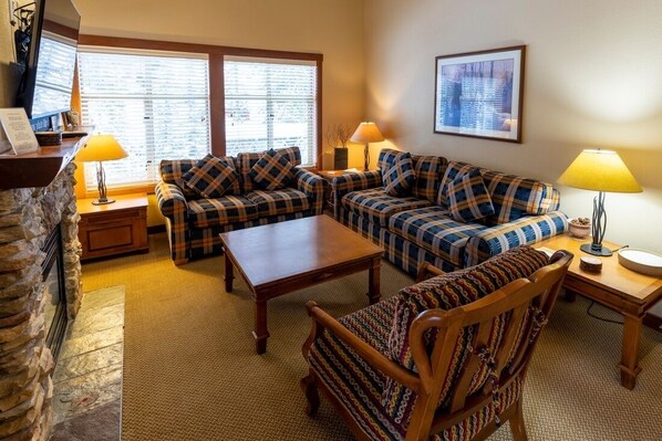 A cozy living room with a stone fireplace, two sofas, a wooden coffee table, and two lamps.