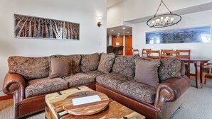 A modern living room with a sectional sofa, a wooden coffee table, and a chandelier. - 1311 - Three Bedroom Deluxe Eagle Springs West 3 Condo (Solitude)