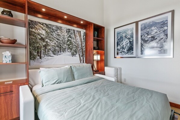 A bedroom with a large bed, wooden shelving, and two framed pictures on the wall.
