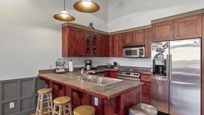 Una cocina moderna con armarios de madera, un refrigerador de acero inoxidable, un microondas y una isla grande con taburetes.