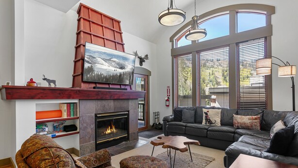 Una sala de estar con chimenea, muebles con diseño, un sofá y ventanas grandes.
