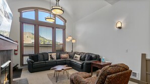 Una sala de estar con un sofá modular, sillones estampados, una chimenea y un ventanal con persianas.