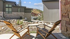 Un patio con dos sillas Adirondack de madera, un muro de piedra y vista a una montaña y edificios al fondo.