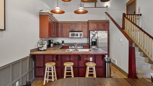 Una cocina con armarios de madera, una isla central con taburetes, un lavamanos de acero inoxidable y un refrigerador de acero inoxidable.
