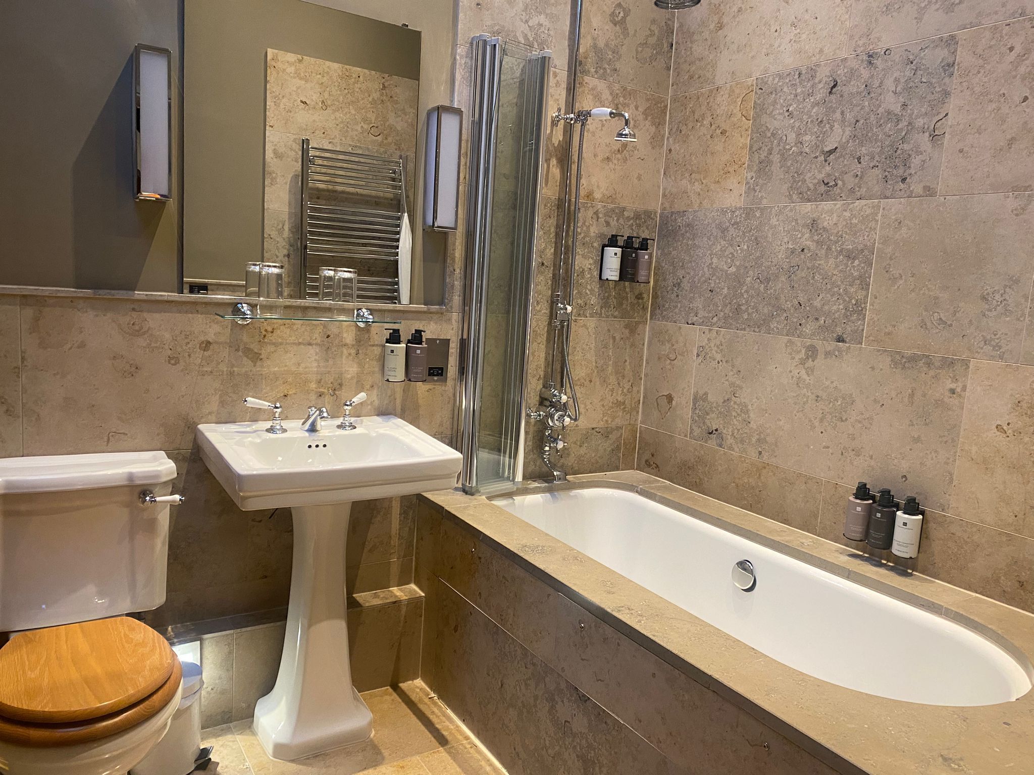 A bathroom with a white pedestal sink, a bathtub, and a toilet with a wooden seat.
