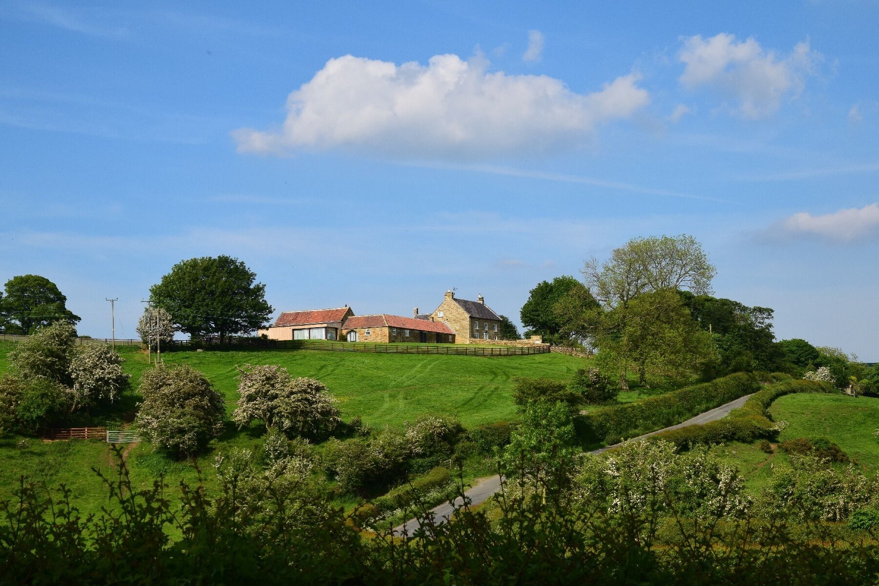 Une maison de campagne aux murs en pierre, entourée d’une végétation luxuriante et sous un ciel dégagé.