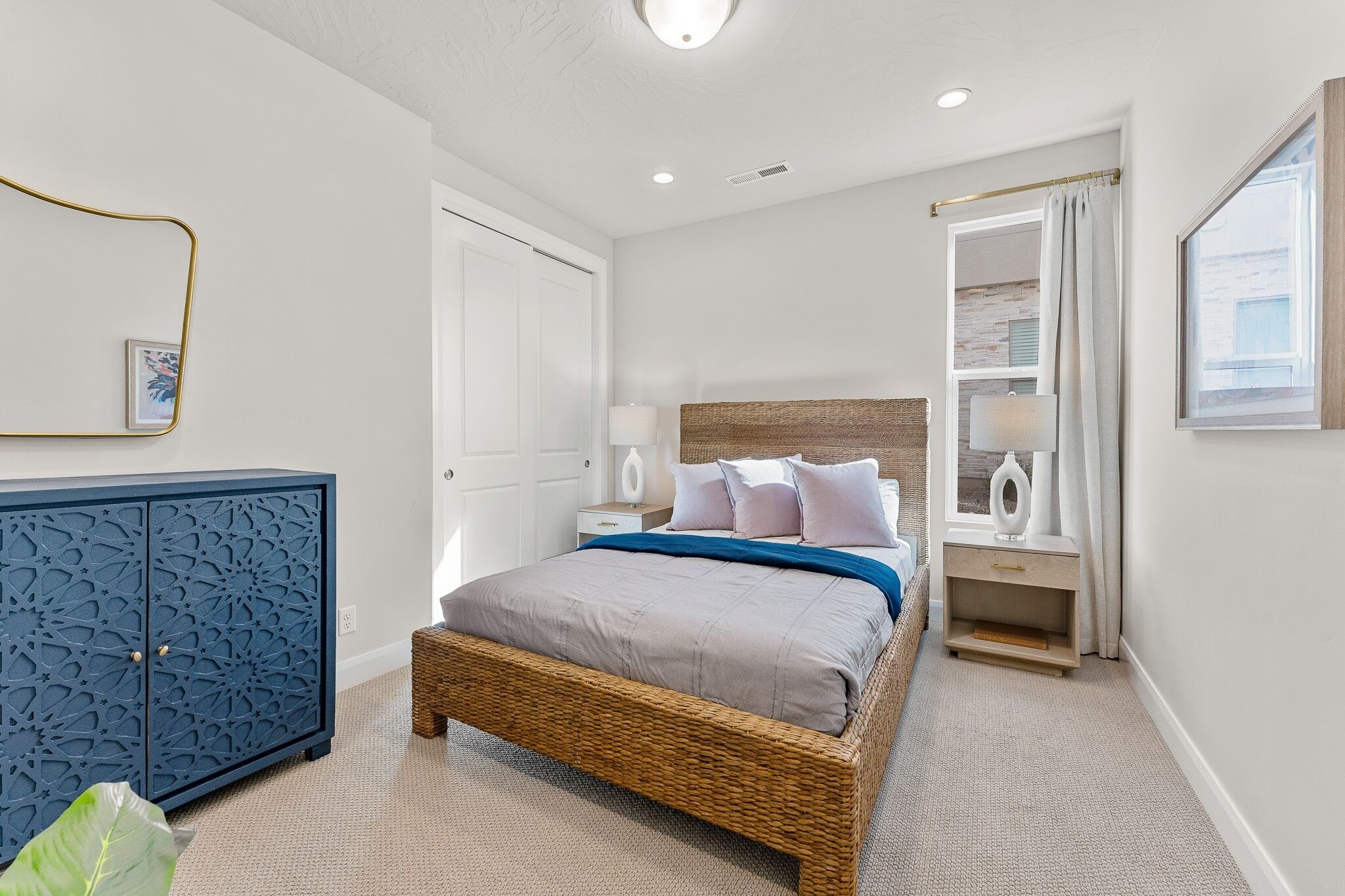 A bedroom with a wicker bed, a blue cabinet, a nightstand, and a window with curtains.