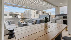 Un patio moderno al aire libre con mesa de madera, zona de estar y una parrilla.