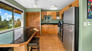 A modern kitchen with wooden cabinets, a stainless steel refrigerator, and a bar area with a glass top. - Kauai Hale Kahanalu 8 2 Bedroom Condo (Koloa)