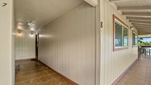 A corridor with a tiled floor, white walls with vertical paneling, and a window with a red frame. - Kauai Hale Kahanalu 8 2 Bedroom Condo (Koloa)
