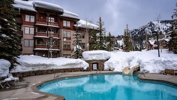 Relax by the resort pool surrounded by snow-covered buildings with lounge chairs and a nearby structure.
