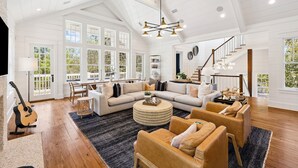 A spacious living room with a large sectional sofa, a round coffee table, and a dining area with a table and chairs. - Watersound Beach! With Carriage House, Private Pool, LSV/Golf Cart, & 4 Bikes! (Watersound)