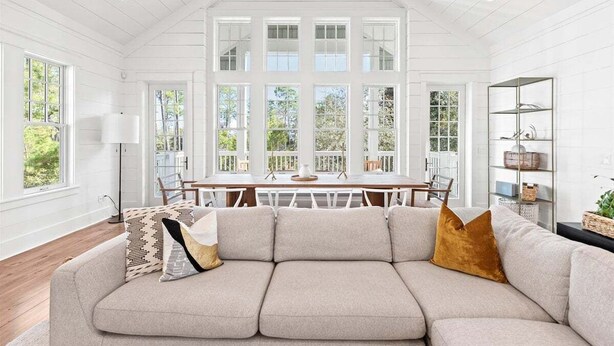 A spacious living room with a large sectional sofa, a dining table, and a view of the outdoors through large windows. - Watersound Beach! With Carriage House, Private Pool, LSV/Golf Cart, & 4 Bikes! (Watersound)